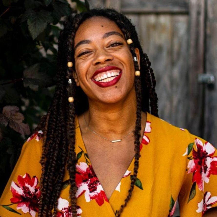 Chandler J. Zolliecoffer, a clinical psychology researcher at the University of Wisconsin-Milwaukee, smiling outdoors in a vibrant yellow floral dress with long braided hair.