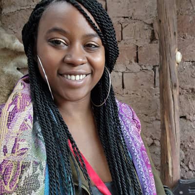 Lisa Brown, a woman with braided hair, smiles with a colorful shawl.