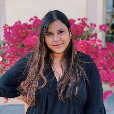 Shabeba Islam, a woman with long brown hair, poses in front of pink bougainvillea flowers.